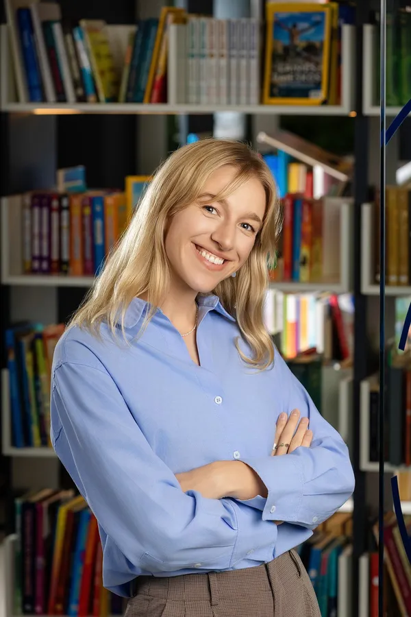 Šypsančios moters portretas mėlynais marškiniais biuro bibliotekoje